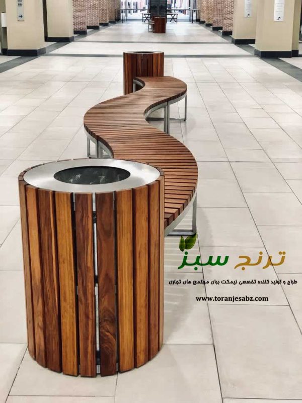 نیمکت منحنی شکل از رویه چوب ترمو و پایه فلزی به همراه سطل زباله در داخل مجموعه تجاری و رفاهی و تفریحی